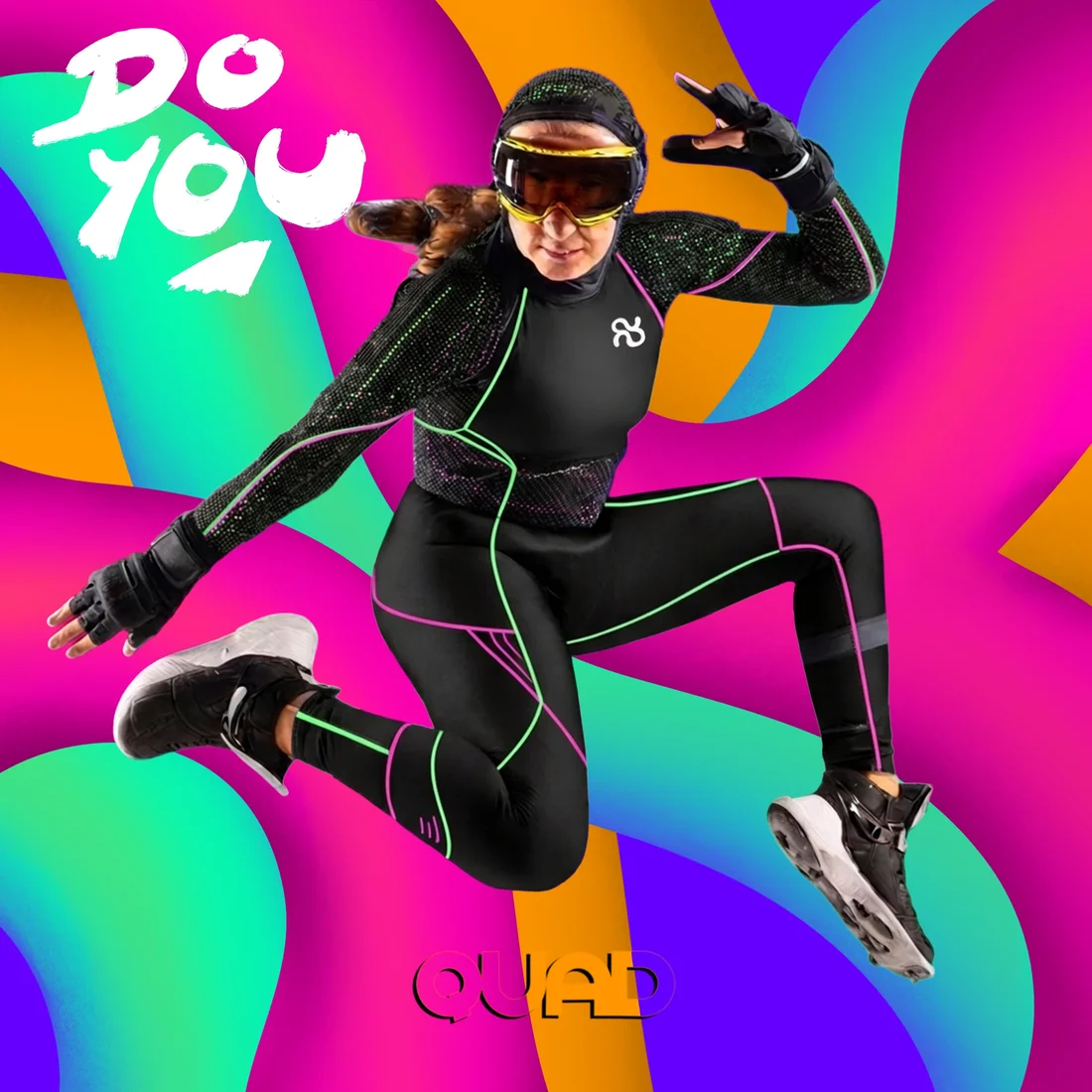 A QUAD athlete leaping mid-air in black kit with mint and pink trim, yellow goggles and the QUAD mark on the chest, over a wavy rave-colour background, a white DO YOU in the corner